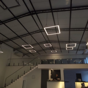 espaço para eventos bem iluminado, aconchegante e grande com lampadas quadradas de LED suspensas, área de bar-man, escada com parapeito em vidro, cozinha entregada e piso de cimento queimado