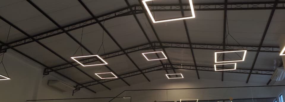 espaço para eventos bem iluminado, aconchegante e grande com lampadas quadradas de LED suspensas, área de bar-man, escada com parapeito em vidro, cozinha entregada e piso de cimento queimado