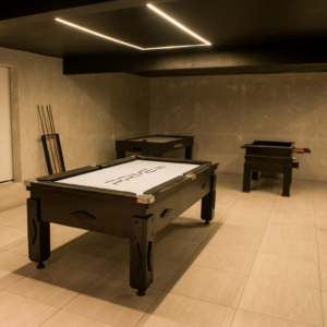 Sala de jogos de um salão de festas com sinuca, totó, outros brinquedos e sofá